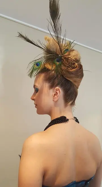 Chignon haut artistique orné de plumes de paon, vu de profil.