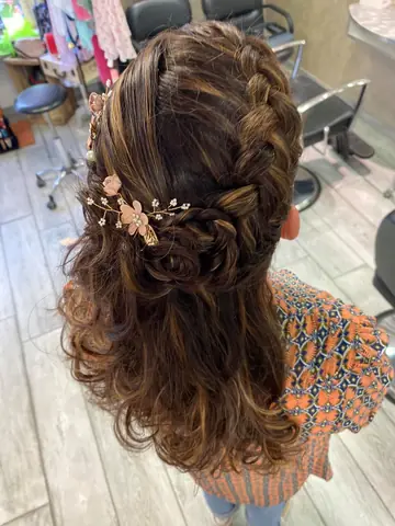 Demi-attache tressée sur cheveux bruns ondulés, ornée de fleurs roses.