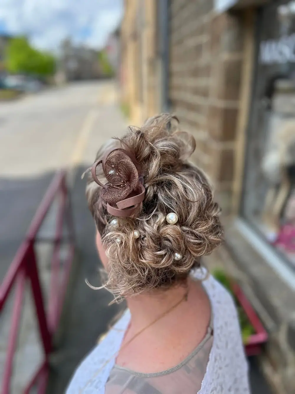 Chignon bouclé orné de perles et d’un accessoire bordeaux, photographié devant le salon.